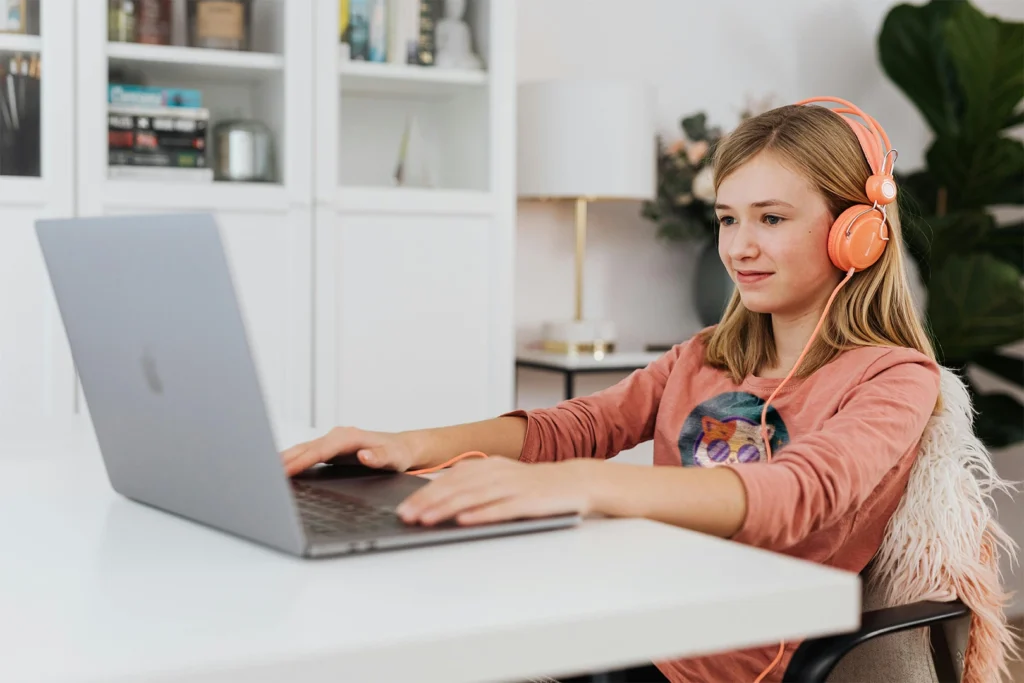 Teenage girl wearing orange headphones, learning happily from the Math Angel platform on her laptop.